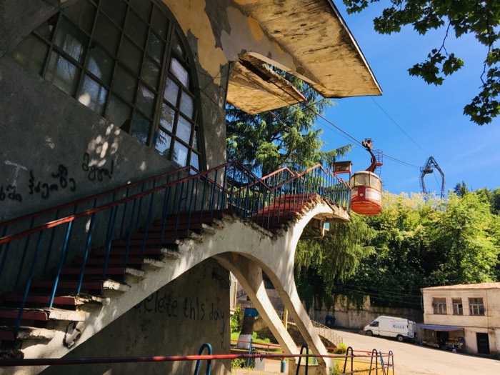 Decaying cable-car station with sweeping concrete stairs and red kanatebi cabin