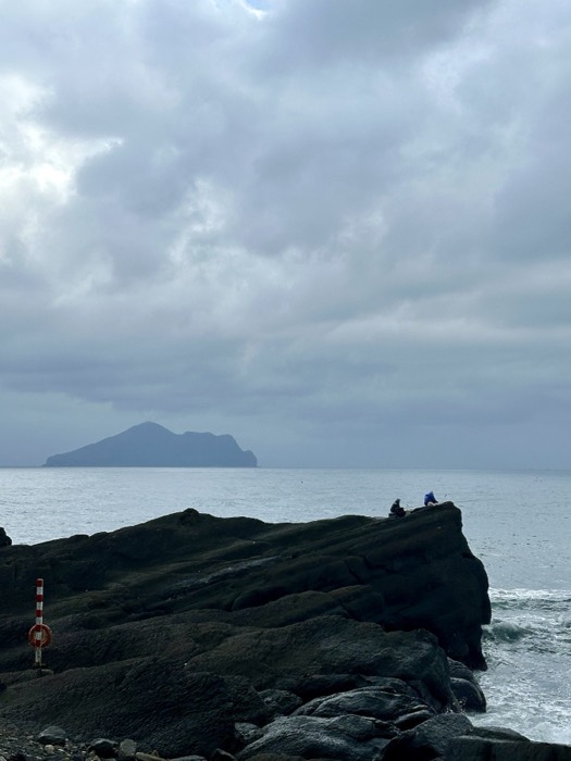 Anglers on rocks with Guishan Turtle Island silhouette across the sea