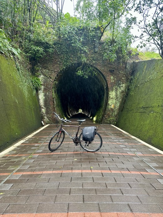 Loaded touring bike parked at mouth of old brick tunnel, rain dripping