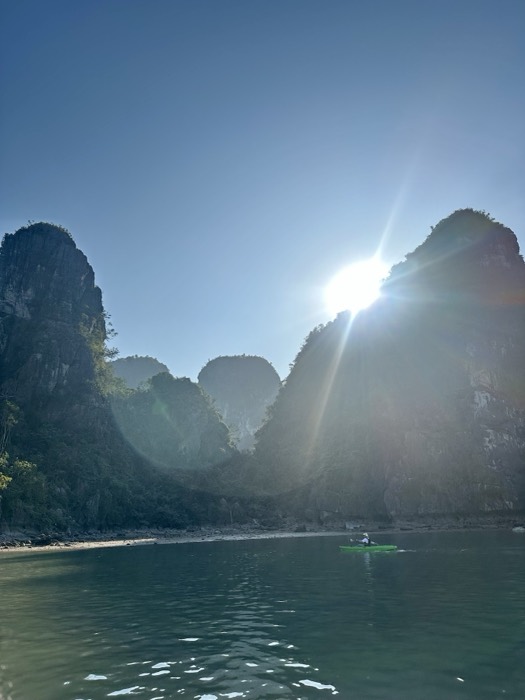 Lone kayaker under sunburst between towering karst peaks, dramatic backlight