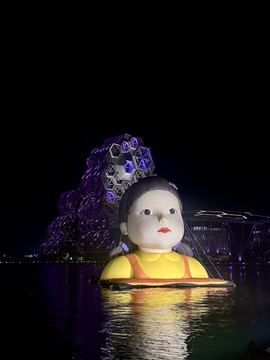 Giant lit Squid Game doll on water beside Kaohsiung Pop Music Center