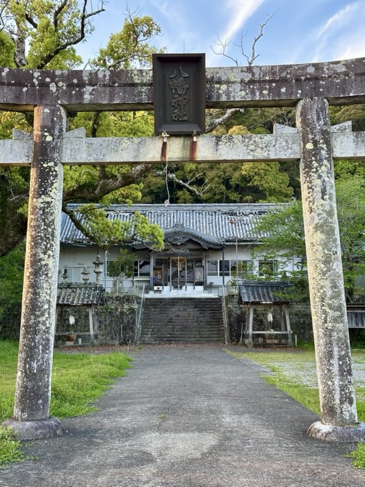 Weathered stone torii framing a tiled-roof shrine and forest.