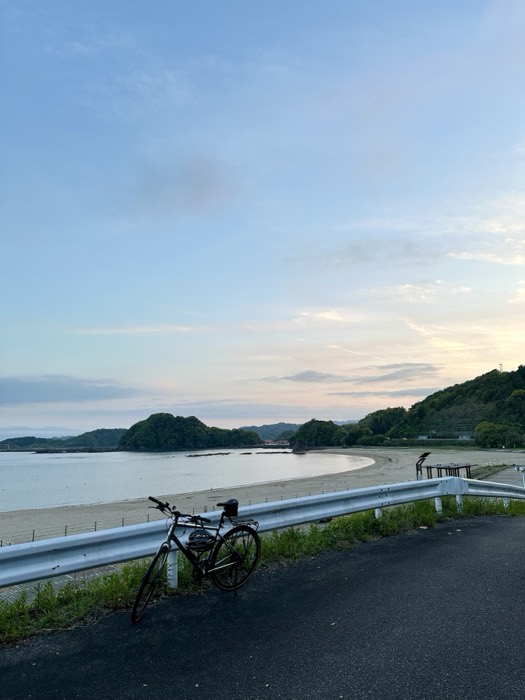 Touring bike against guardrail over crescent beach bay at dusk