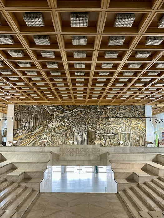 Socialist-modernist gilded mosaic mural under coffered ceiling, monumental interior