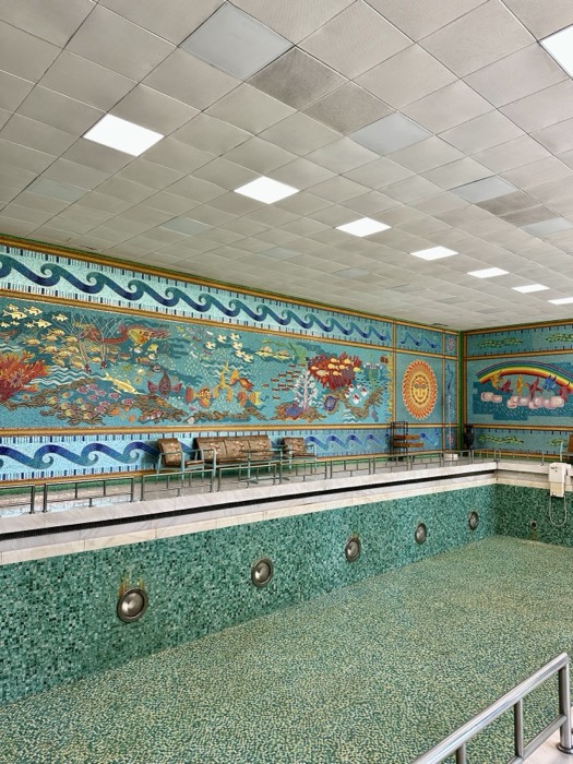 Retro indoor pool with vivid underwater-scene mosaic frieze, green tiles
