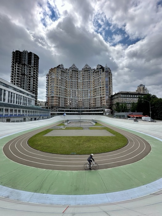 Lone cyclist on velodrome track below dramatic clouds and apartment towers