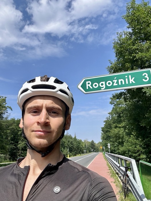Joshua: cycling selfie in helmet beside Rogoznik road sign, blue sky