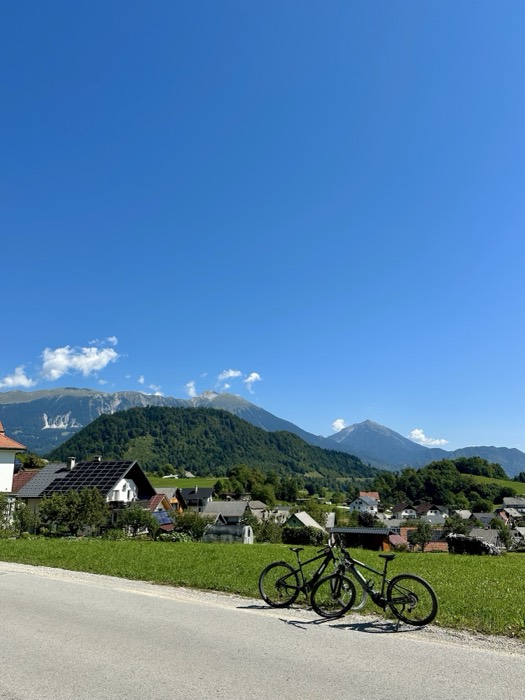 Two bikes parked on road, Slovenian village and Karavanke peaks behind
