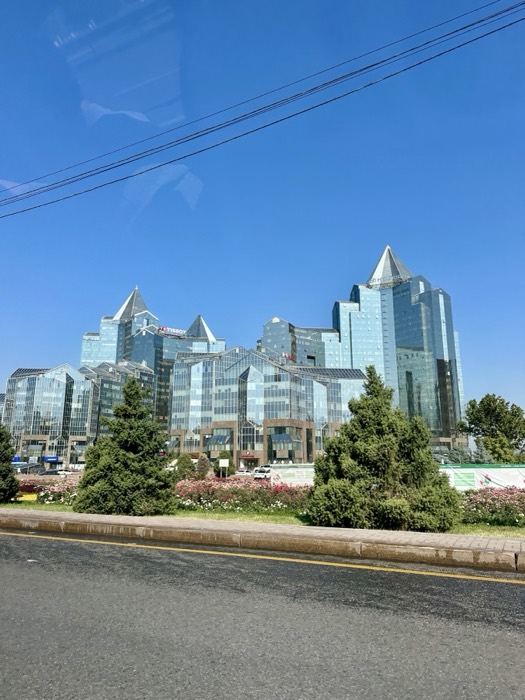 Almaty glass towers with TISSOT sign shot through car window, wires across sky