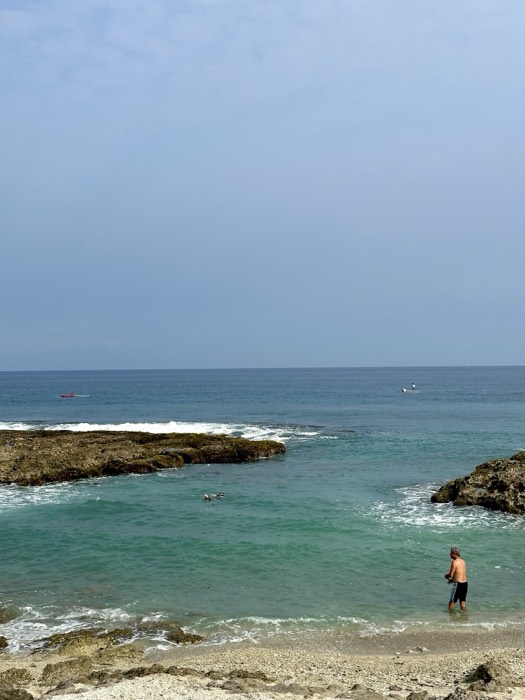 Rocky coastline tidal pool with swimmer and man, overcast