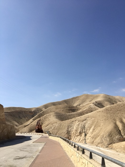 Sculpture beside winding road through tan Judaean Desert hills