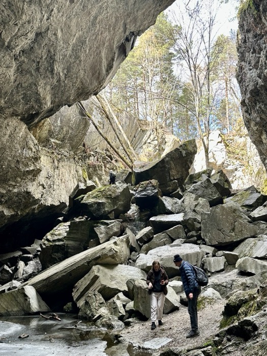 Two people exploring dramatic boulder-strewn rock cave in forest