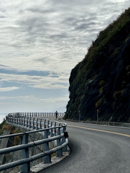 Edited duplicate of lone cyclist on cliff road by rock face