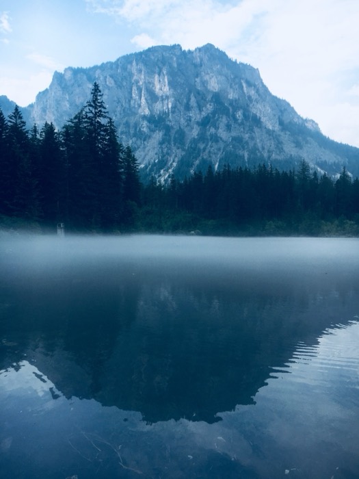 Misty alpine lake mirroring craggy peak at dawn