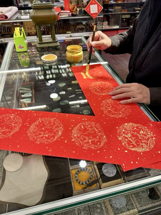 Artisan painting gold New Year couplets on red paper over jade display case