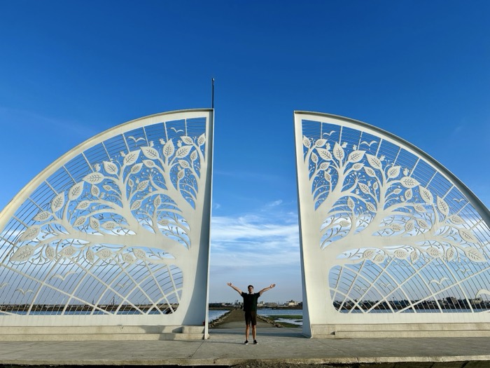 Joshua: edited duplicate, arms wide between white tree-of-life sculpted gates