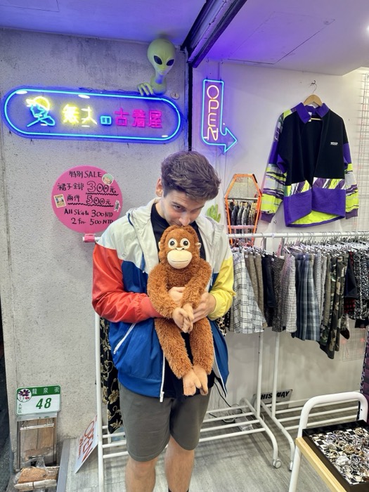 Joshua: hugging plush monkey at neon-lit vintage clothing shop