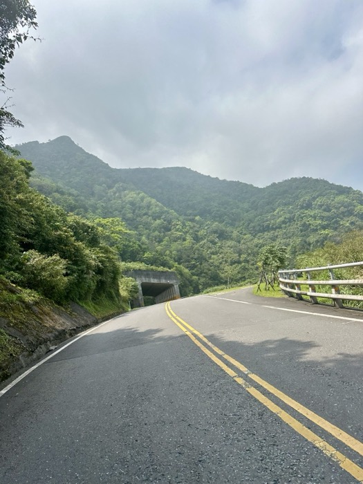 Edited mountain road curving to tunnel under cloudy peaks, Taiwan