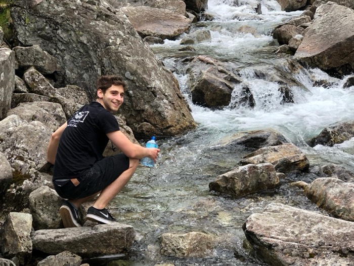 Joshua: crouched filling water bottle from rocky mountain stream on hike
