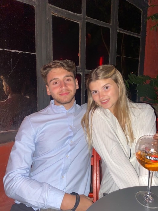 Joshua: posed with a girl at red-lit bar table, spritz glass.