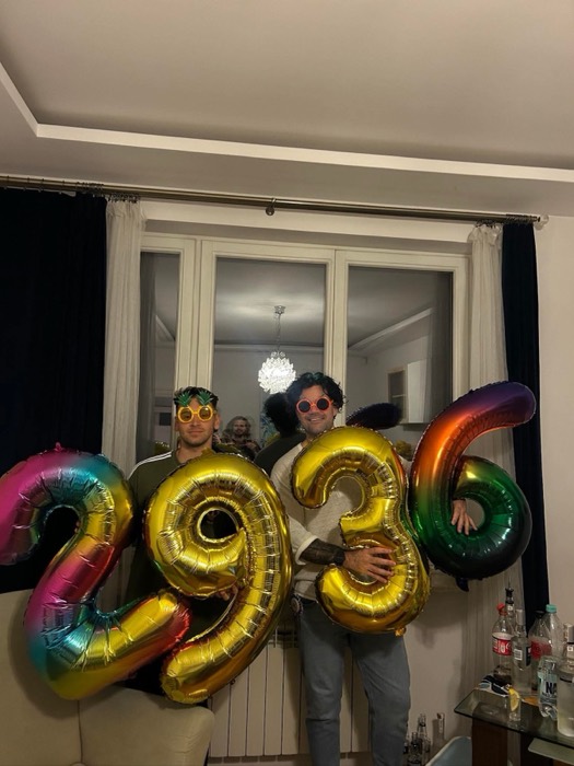 Joshua: with friend holding giant rainbow balloons, pineapple glasses, party