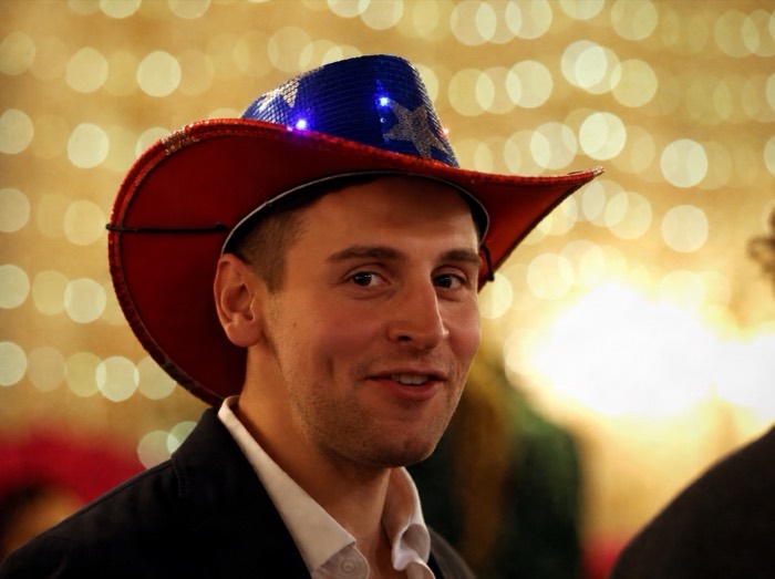 Joshua: grinning in light-up sequin cowboy hat against golden bokeh