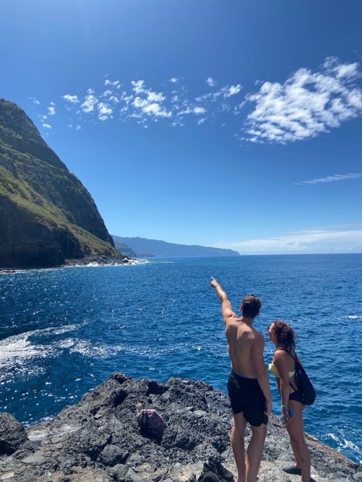 Joshua: shirtless with friend pointing across blue ocean at green cliffs
