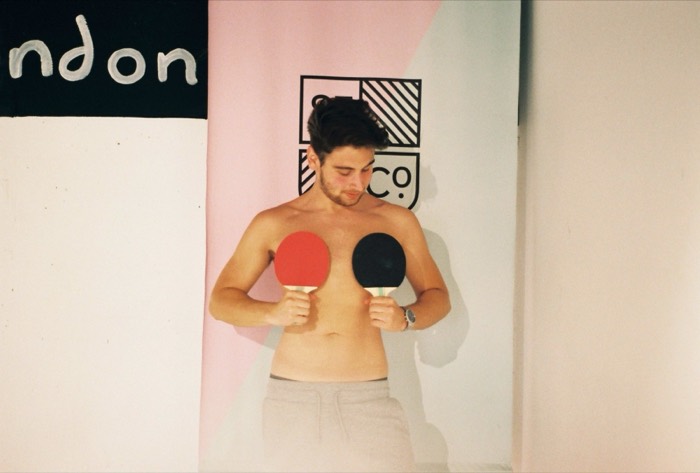 Joshua: shirtless film portrait holding ping-pong paddles, 'London' backdrop.